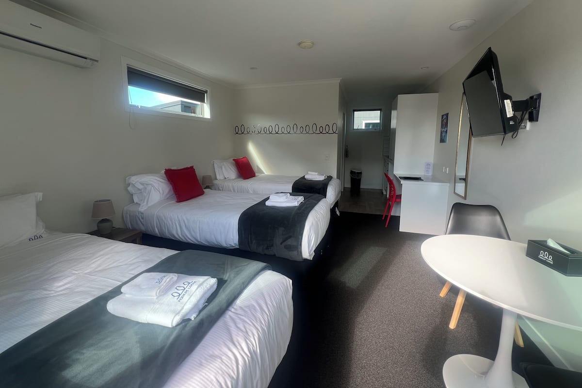 A hotel room with two beds, a desk, a chair, a TV, and a window.