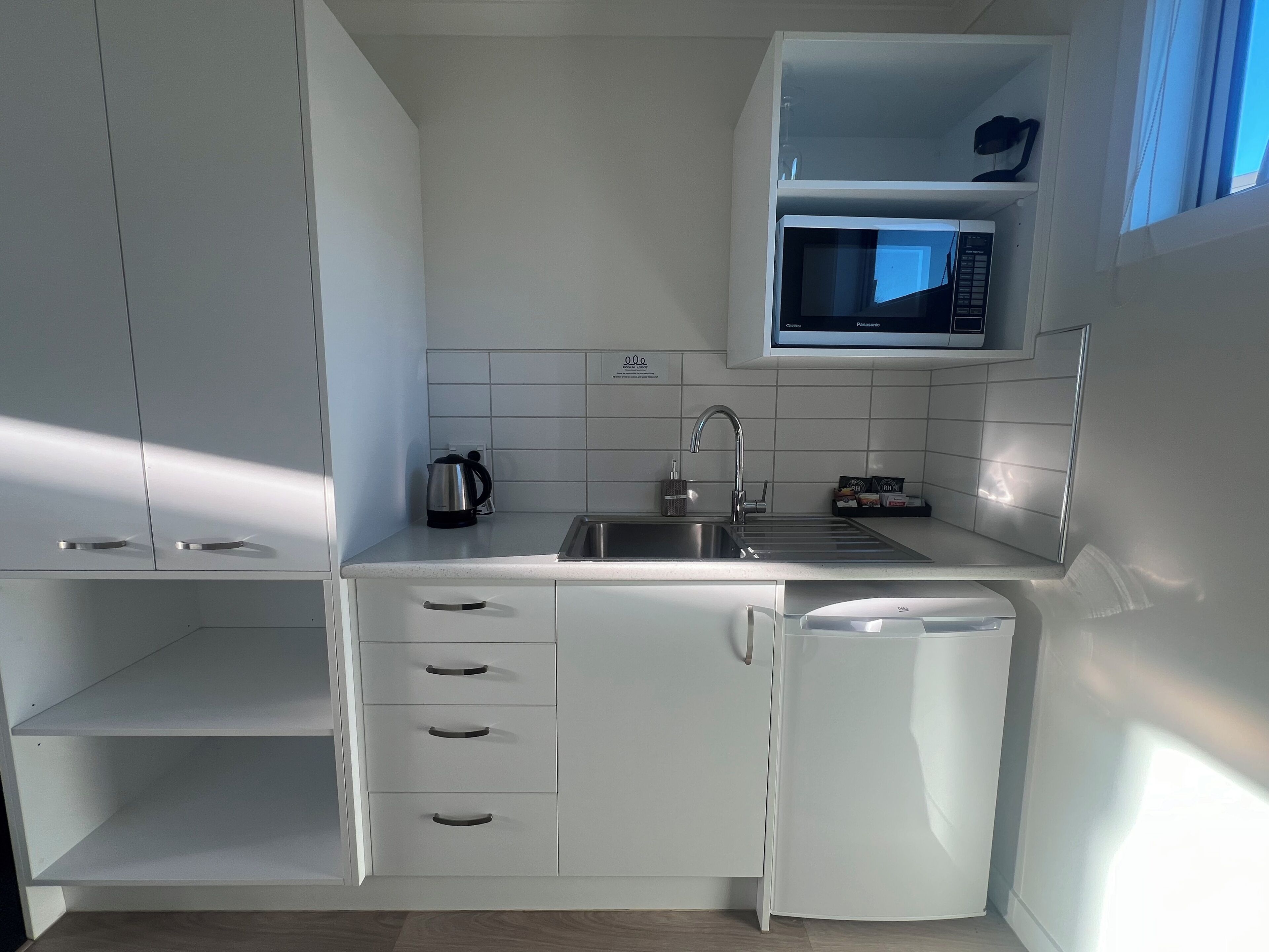 Une cuisine moderne avec des meubles blancs, un four à micro-ondes encastré, une bouilloire et un lave-vaisselle.