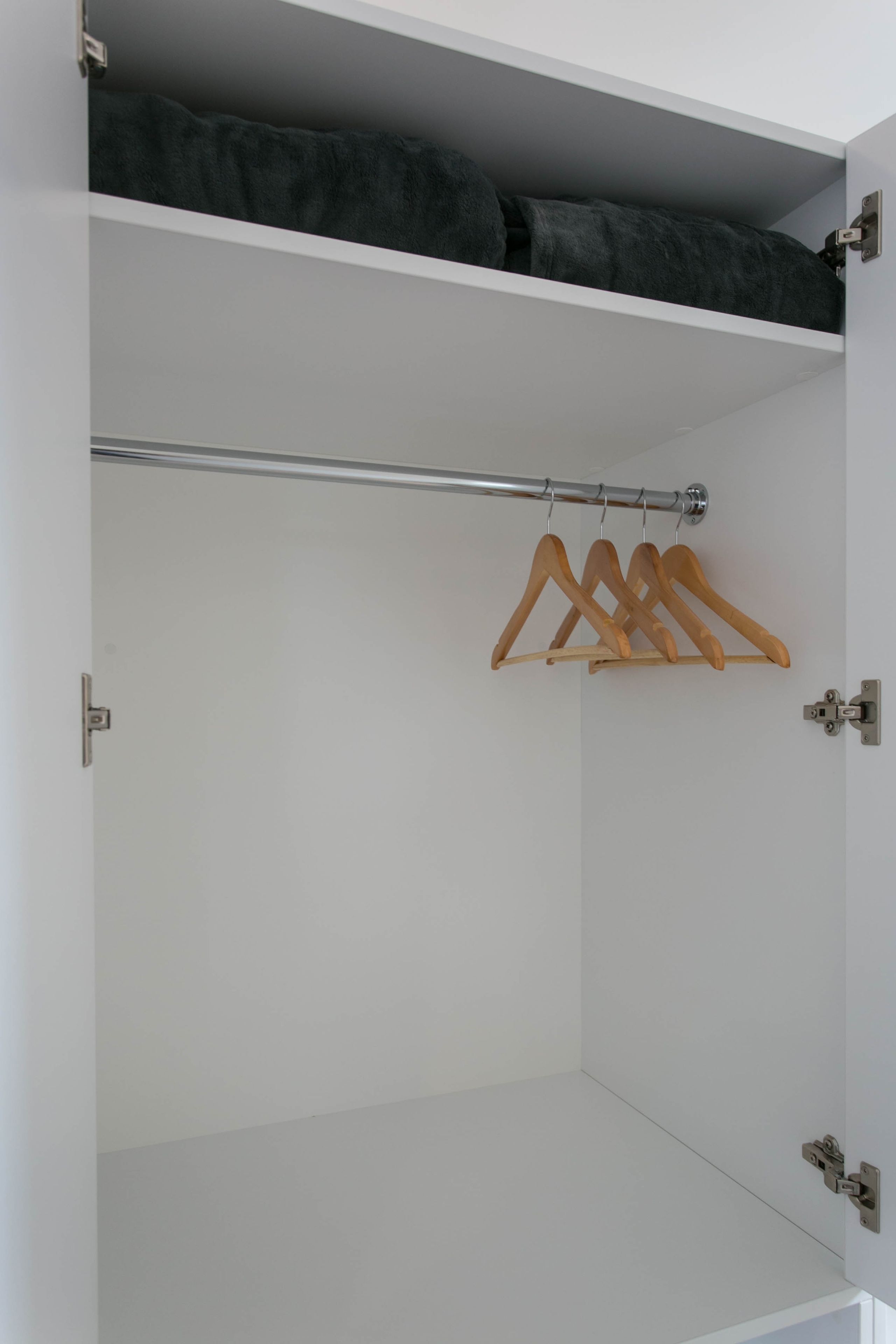 A white wardrobe with a hanging rod and a dark-colored top shelf.