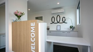 A reception desk with a 'WELCOME' sign, a vase of flowers, and a modern kitchen area in the background. - Podium Lodge (Cambridge)