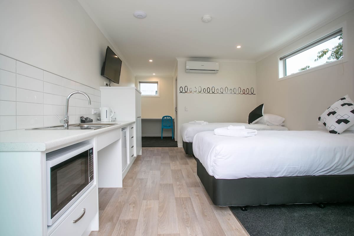 A compact hotel room with a kitchenette, a bed, a window, and a wall-mounted TV.