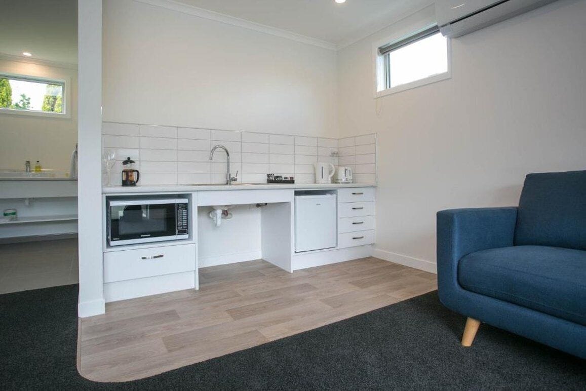 A modern kitchen with white cabinetry, a microwave, and a coffee maker. There is a blue sofa in the living area.