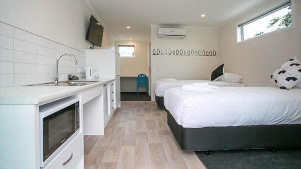 A compact hotel room with a kitchenette, a bed with white bedding, a small bathroom, and a window providing natural light.