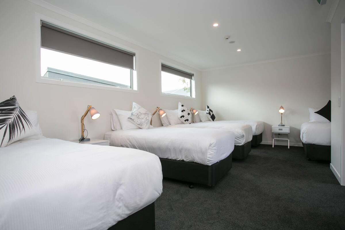 A hotel room with three beds, a small desk, and two windows.