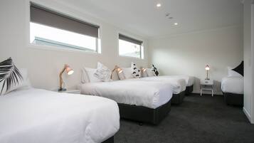 A hotel room with three beds, a small desk, and two windows.