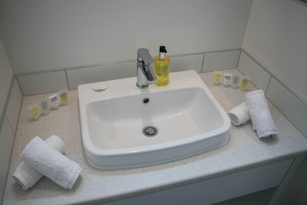 A bathroom sink with a faucet, a bottle of yellow liquid, and several toiletries on the countertop.