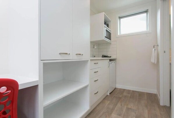A compact kitchen with white cabinetry, a window, and a red chair.