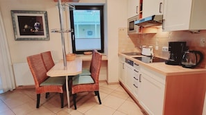Una cocina compacta con comedor, que incluye una mesita y dos sillas, un microondas, una cafetera y vistas a un balcón a través de una ventana.