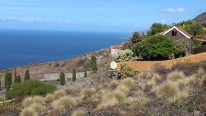 Ein Küstenhaus mit Steinziegeldach, umgeben von trockener Vegetation und Blick aufs Meer.