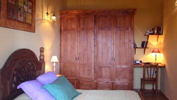 Quarto com um grande armário de madeira, uma cama com cabeceira, duas luminárias de cabeceira e uma pequena mesa com uma luminária e livros.