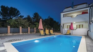 A swimming pool with lounge chairs and umbrellas, surrounded by a paved area and a building with a balcony. - Awesome home in Pakostane (Pakostane)