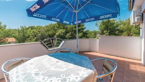 A balcony with a table and chairs, a blue umbrella, and a view of trees and buildings. - Awesome home in Pakostane (Pakostane)