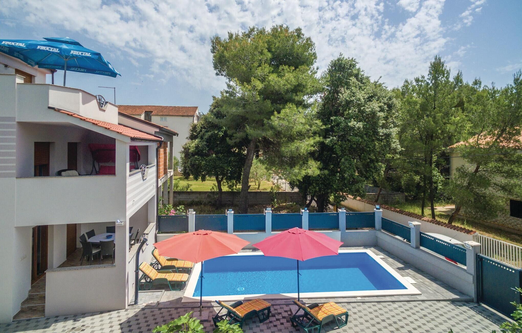 Un área de piscina con una piscina azul, sombrillas rojas y sillones de descanso.