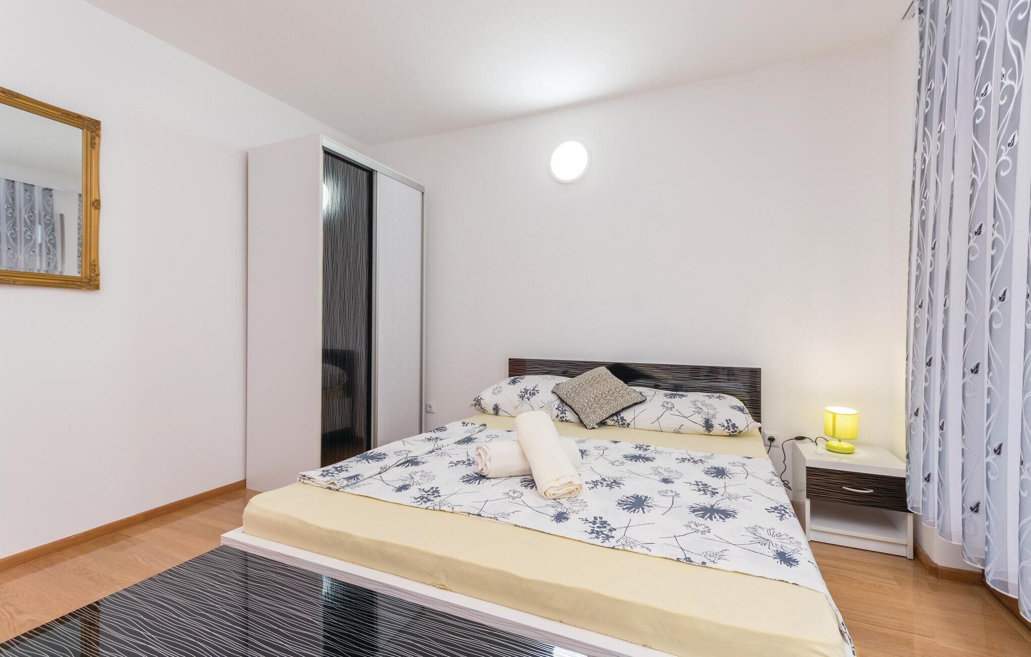 A bedroom with a bed, a nightstand, a lamp, a mirror, and a wardrobe.