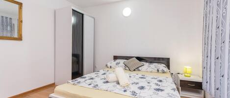 A bedroom with a bed, a nightstand, a lamp, a mirror, and a wardrobe.