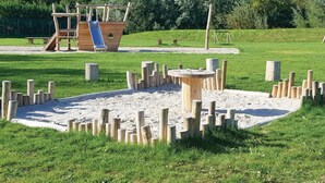 A playground with a slide, climbing structures, and a sandpit surrounded by wooden posts.