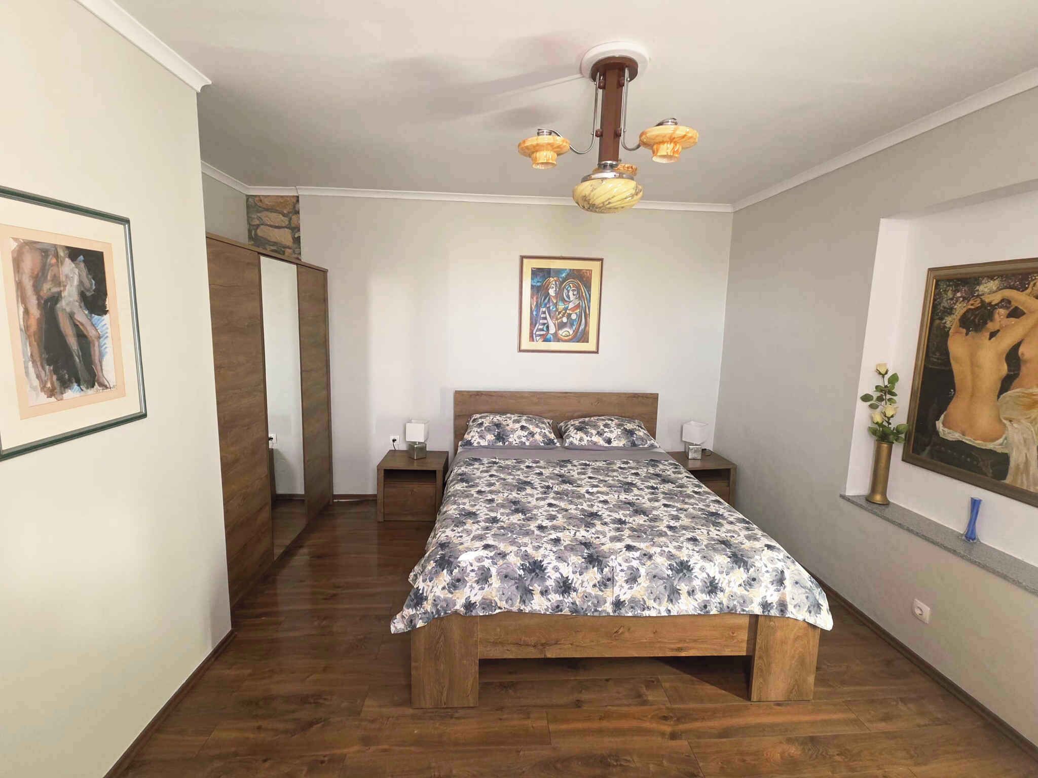 Une chambre à coucher avec un lit en bois, un ventilateur de plafond et des œuvres d’art accrochées aux murs.
