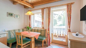 A cozy room with a wooden bench, a table, and a chair. There is a window with curtains, a wall-mounted TV, and a small table with a vase. - Ferienwohnung - Hoch Pustertal (Kartitsch)
