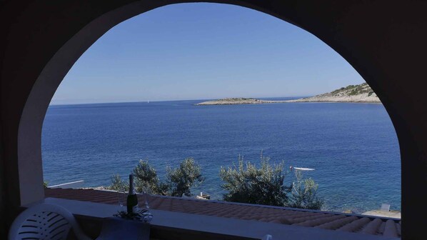 A view through an arched window overlooking a calm sea, with a small island and rocky shoreline in the distance.