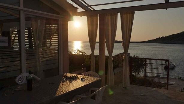 A balcony with a table and chairs, overlooking a body of water during sunset. - Holiday apartment for 4 people directly by the sea (Ražanj)