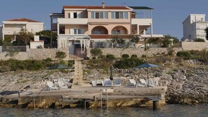 A coastal property with a large house, a stone retaining wall, and a pool area with lounge chairs. - Holiday apartment for 4 people directly by the sea (Ražanj)