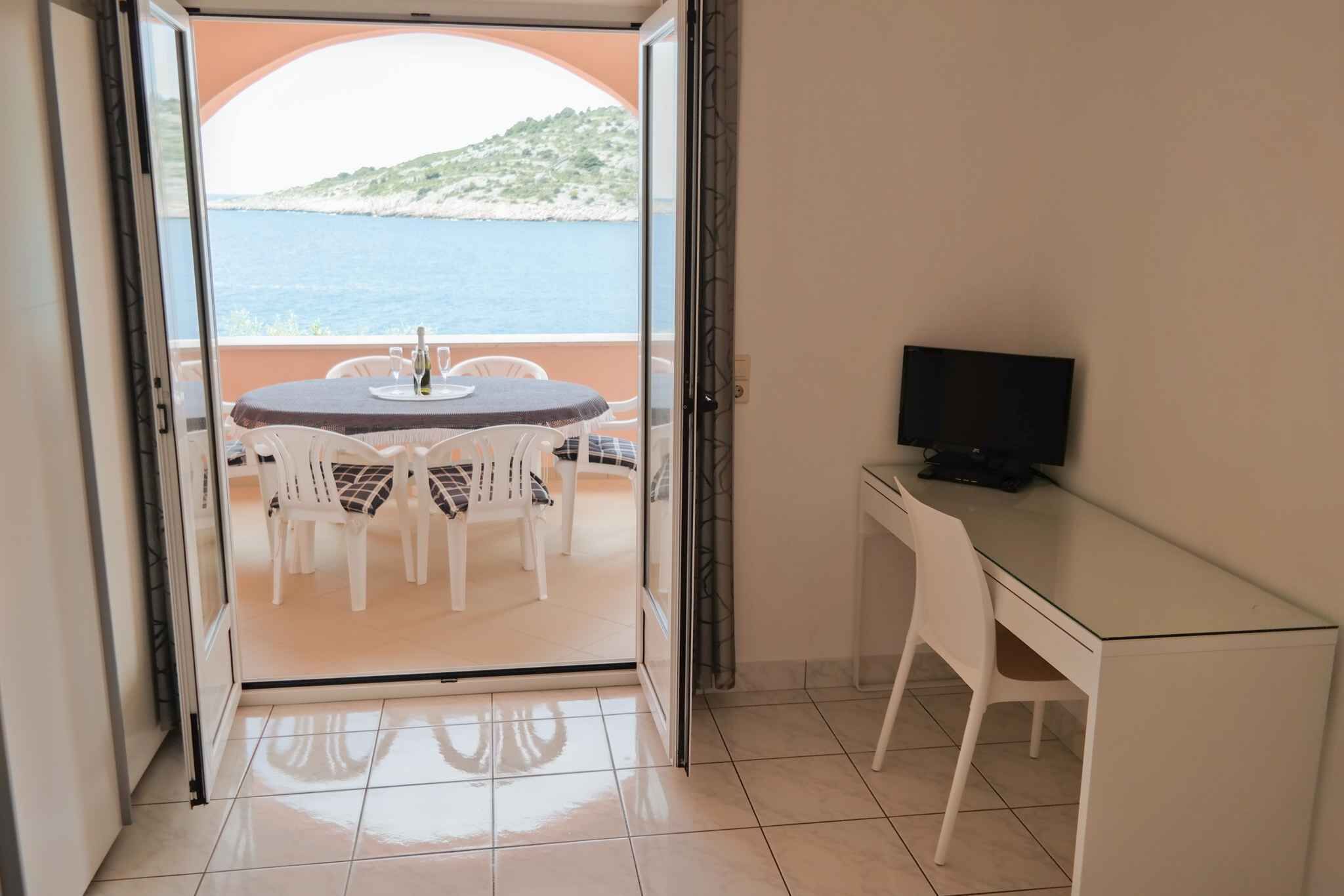 A room with a balcony, a table with chairs, a TV on a desk, and a view of the sea.