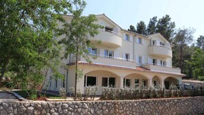 A multi-story building with balconies, a stone wall in front, and a clear sky. - Holiday apartment with air conditioning only 40 m from the beach (Malinska)