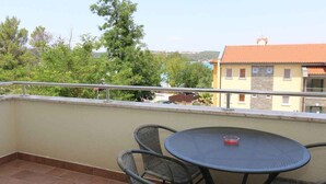 A balcony with a round table and wicker chairs, overlooking a building with a tiled roof and trees. - Holiday apartment with air conditioning only 40 m from the beach (Malinska)