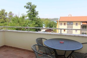 Un balcone con un tavolo rotondo e sedie in vimini, affacciato su un edificio con tetto in tegole e alberi.