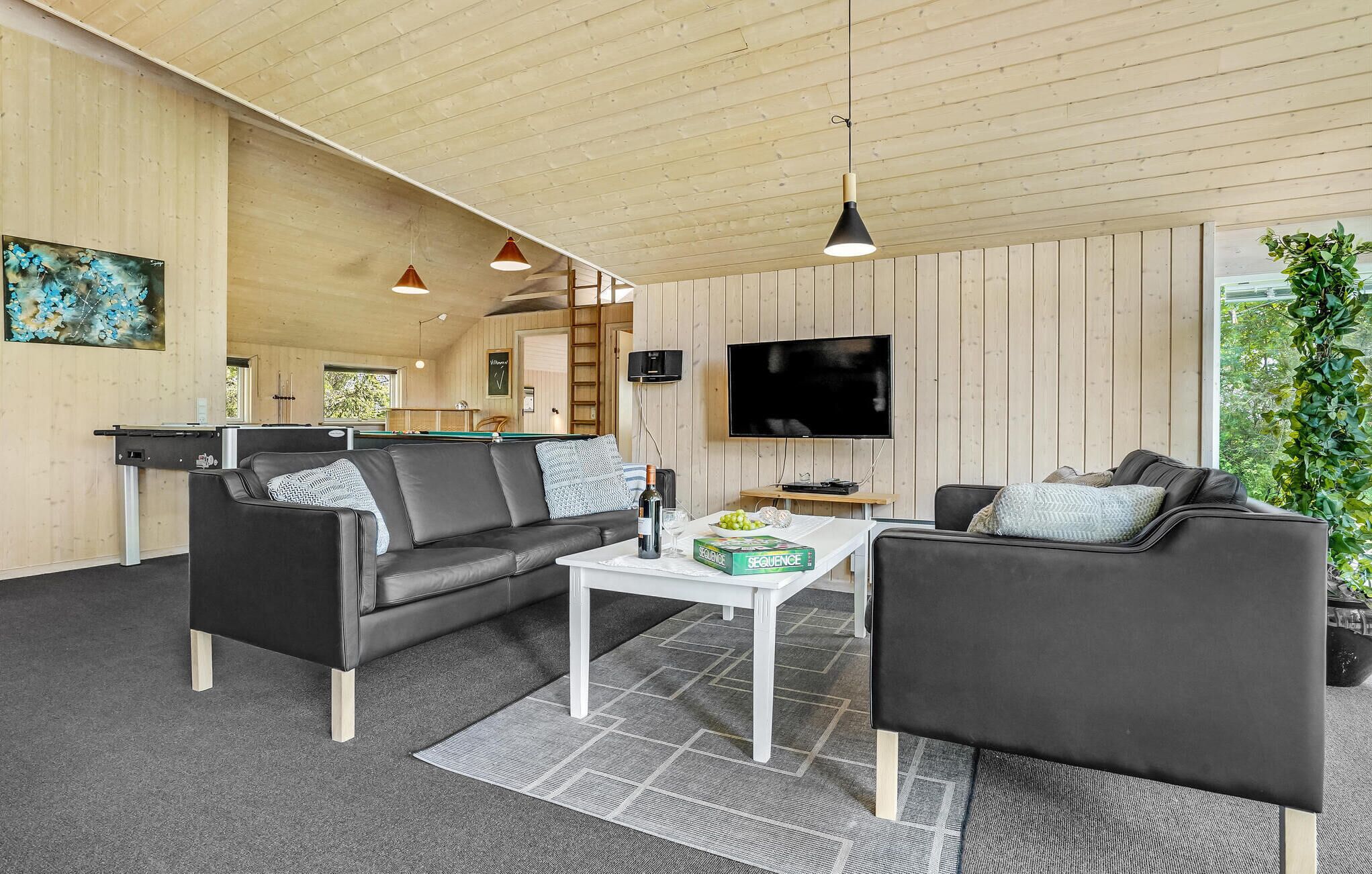 A modern living room with a pool table, two sofas, a coffee table, and a TV.