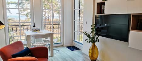 A modern kitchen with large windows, a flat-screen TV, and a dining area with a table and chairs.
