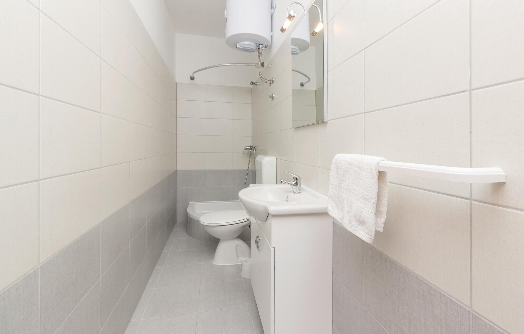 A narrow bathroom with white tiles, a toilet, a sink, and a towel rack.
