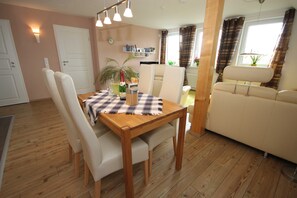 A dining area with a wooden table, white chairs, a checkered tablecloth, and a bottle of champagne. - Möwennest - FW Möwennest (Ahrenshoop)