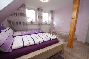 A bedroom with a bed, a window with curtains, a radiator, and a wooden floor. - Möwennest - FW Möwennest (Ahrenshoop)