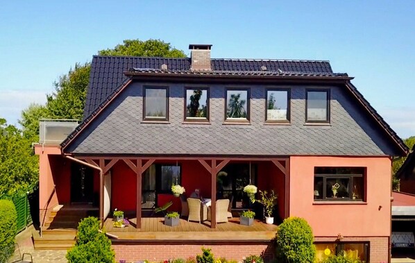 A house with a sloped roof, a covered porch with seating, and a brick foundation. - Möwennest - FW Möwennest (Ahrenshoop)