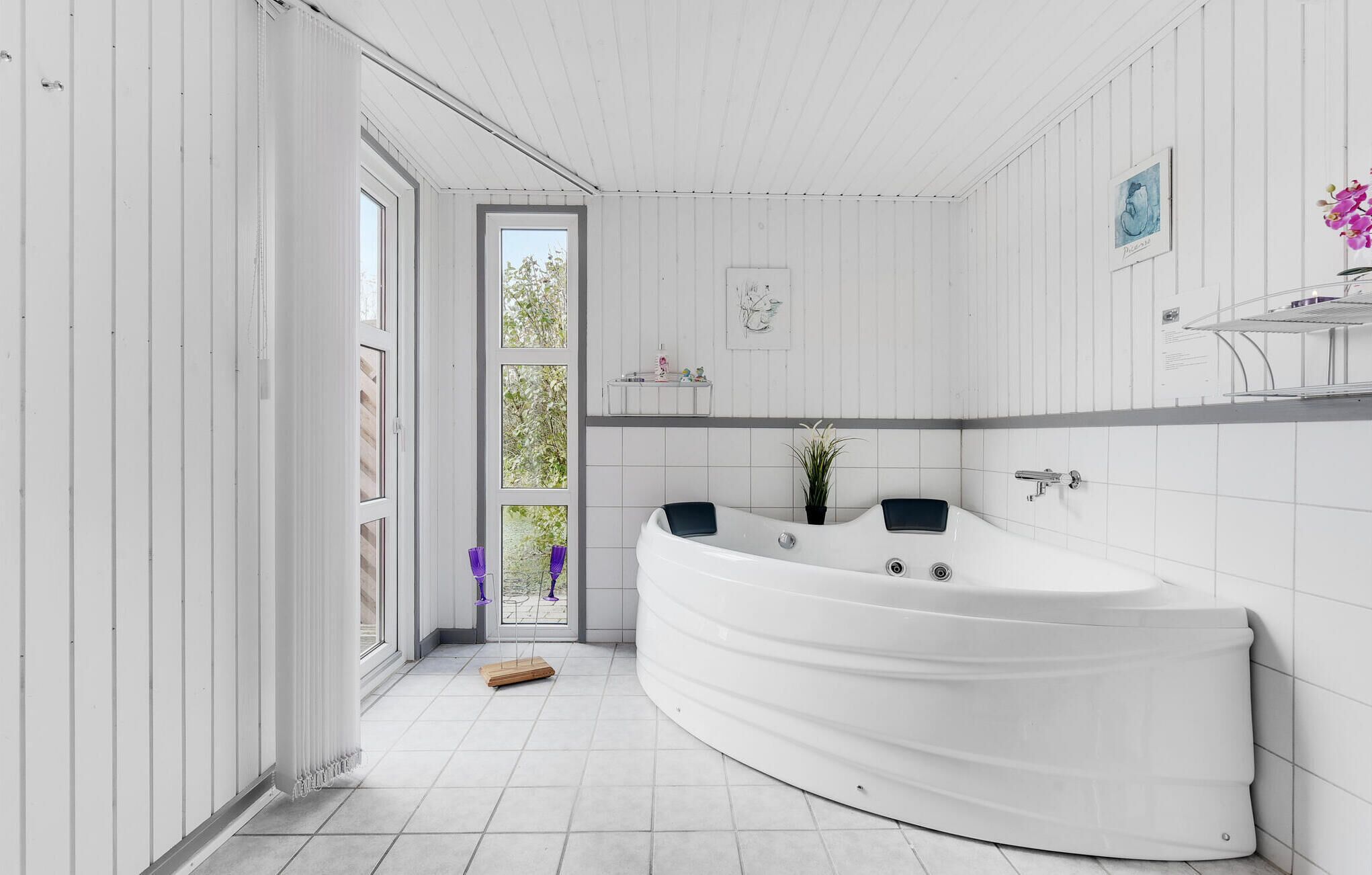 Un baño moderno con una bañera independiente grande, paredes cubiertas de azulejos blancos y un ventanal que proporciona luz natural.