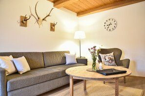 Una sala de estar con un sofá, una mesa redonda de centro, una lámpara, un reloj y calaveras de animales colgadas en la pared.