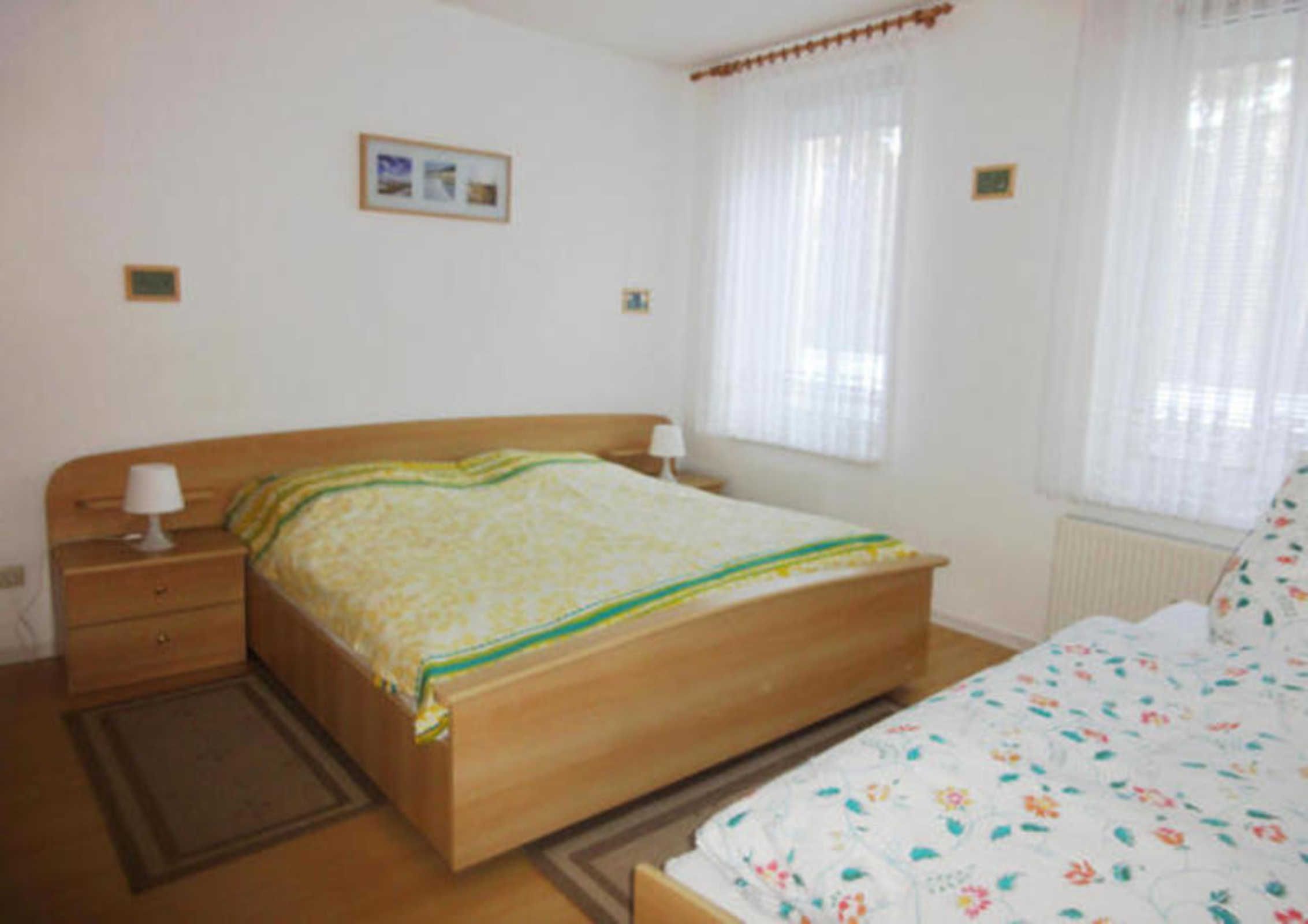 Un dormitorio con cama de madera, una mesita de noche, una ventana con cortinas y un radiador.