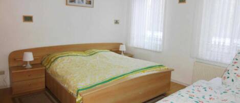 Un dormitorio con cama de madera, una mesita de noche, una ventana con cortinas y un radiador.