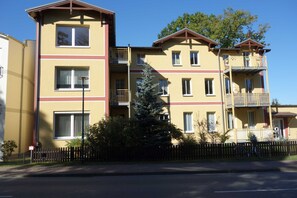 En flervåningsbostadsbyggnad med balkonger, en cykel och ett litet träd i förgrunden.