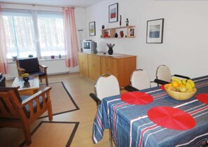 A room with a dining table, chairs, a television, a cabinet, and a fruit bowl.