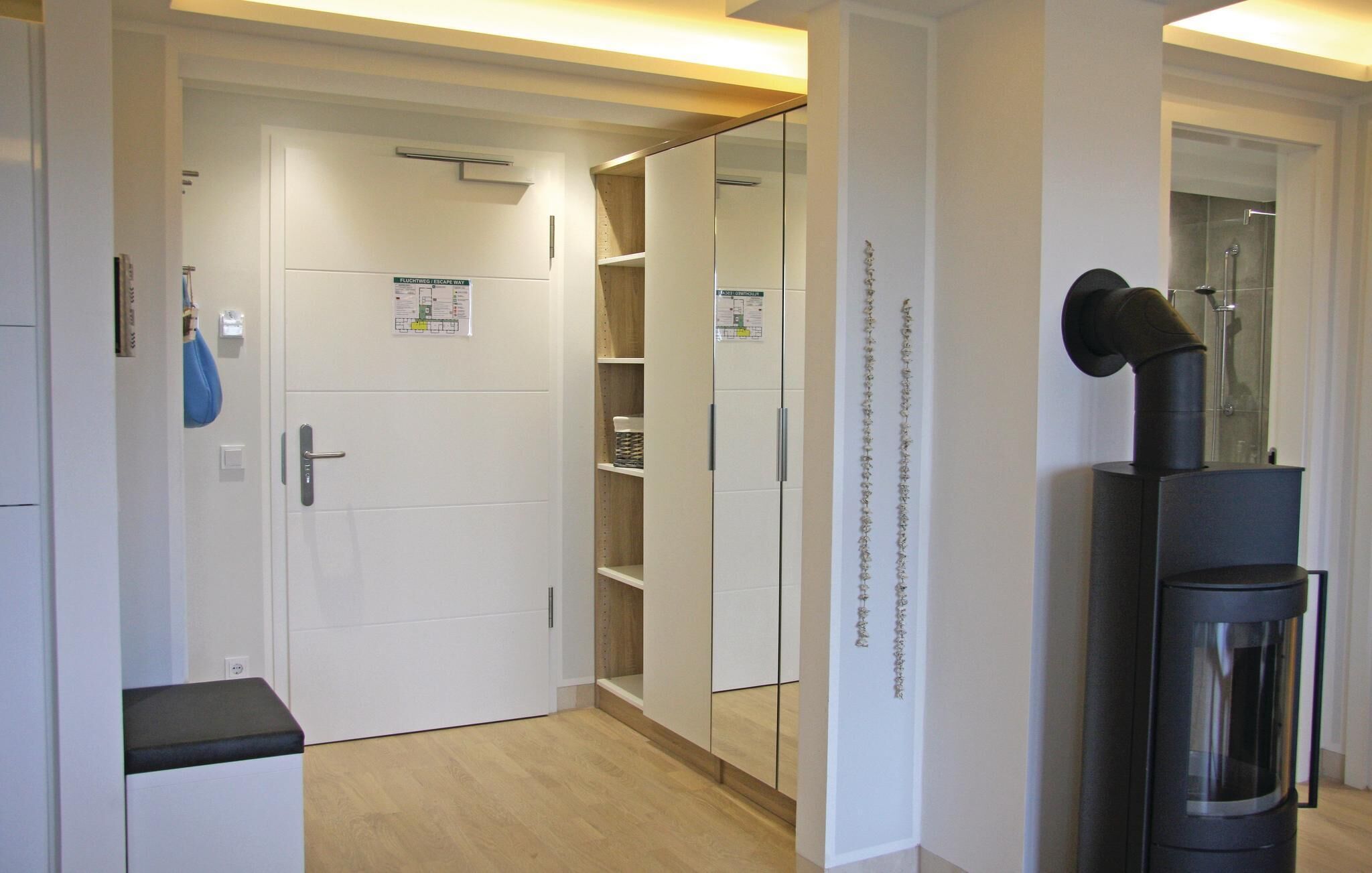 Habitación de hotel con una puerta blanca, un pequeño banco, un espejo y un objeto negro sobre un soporte.