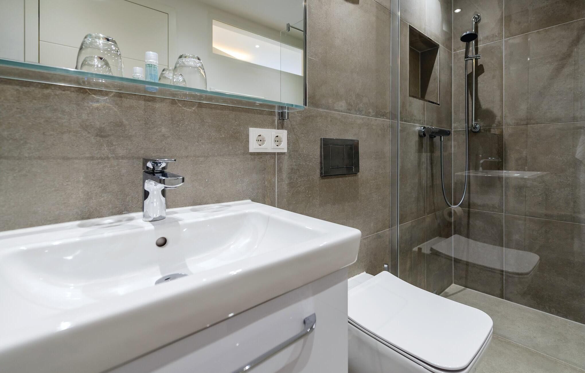 Een moderne badkamer met een wit wastafelmeubel, een douchecabine met glazen wanden en een toilet.