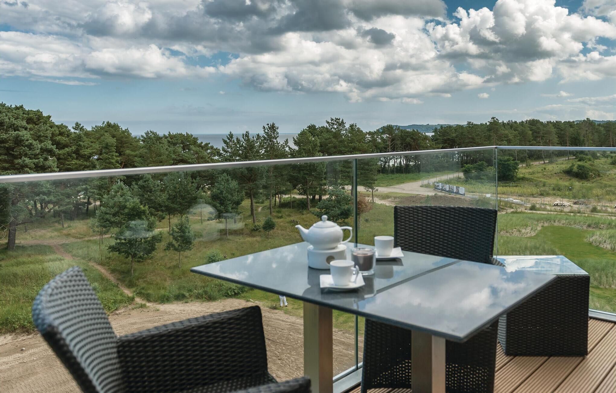 A balcony with a table and chairs, overlooking a landscape with trees and a body of water.