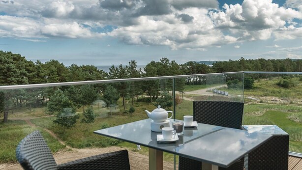 A balcony with a table and chairs, overlooking a landscape with trees and a body of water.