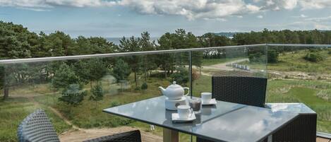 A balcony with a table and chairs, overlooking a landscape with trees and a body of water.