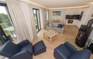 Een moderne woonkamer met een bank, een salontafel en een open haard. Er is een keuken met een fornuis en kasten.