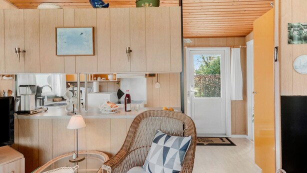 A compact kitchen with wooden cabinets, a dining area with wicker furniture, and a door leading to an outdoor area. - Beautiful home in Stubbekøbing with WiFi (Stubbekøbing)