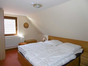 A bedroom with a large bed, a bedside table, a lamp, a radiator, and a window with blinds. - Holiday house 2 - Rügen-Fewo 108/2 (Garz/Rügen)
