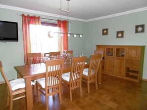 A dining area with a wooden table and chairs, a television mounted on the wall, and a cabinet with glass doors. - Holiday house 2 - Rügen-Fewo 108/2 (Garz/Rügen)